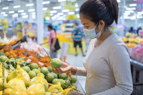 Asian woman wearing a mask shopping fruit in the supermarket during new normal change after coronavirus or post covid-19 outbreak pandemic situation