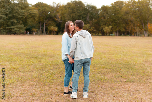 Young cute couple is holding hands and looking at each other outdoors in a park