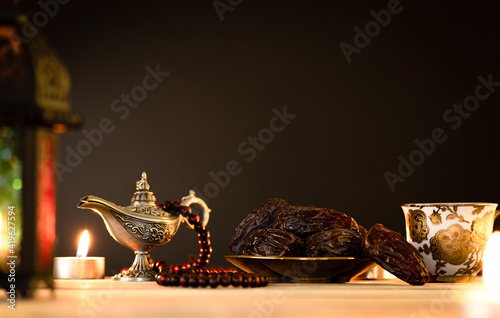 Ramadan food and drinks concept. Ramadan Lantern with arabian lamp, wood rosary, tea, dates fruit and lighting on a wooden table against dark background.