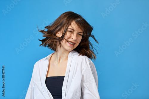 happy young woman with flyaway hair in white shirt on blue background. photo