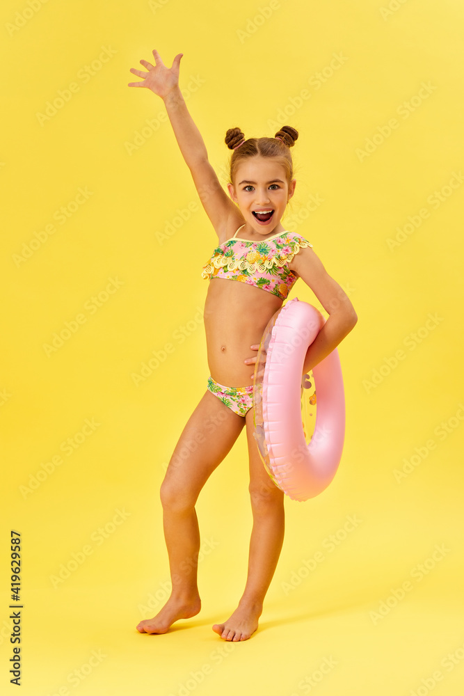 little child girl in swimwear with inflatable rubber ring looking super excited on yellow background little child girl in swimwear with inflatable rubber ring looking super excited on yellow background