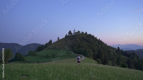 Static shot of a male hiker walking towards the church on top of a hill. Shot at blue hour just before sunrise at Sveti Jakob, Medvode, Slovenia. photo