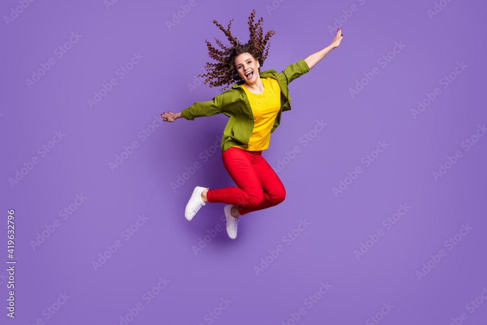 Full size photo of young funky funny smiling cheerful girl jumping with flying hair isolated on violet color background Full size photo of young funky funny smiling cheerful girl jumping with flying hair isolated on violet color background