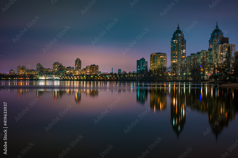Night view of modern buildings in the Obolon district of Kiev, Ukraine, close to the Dnieper River, The lights reflect on the calm water.
