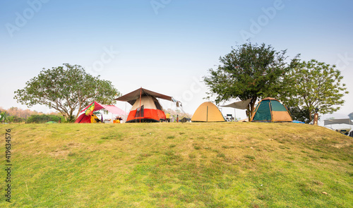 Colorful tents on the pitch, under the trees, the sky and the grass in the morning.