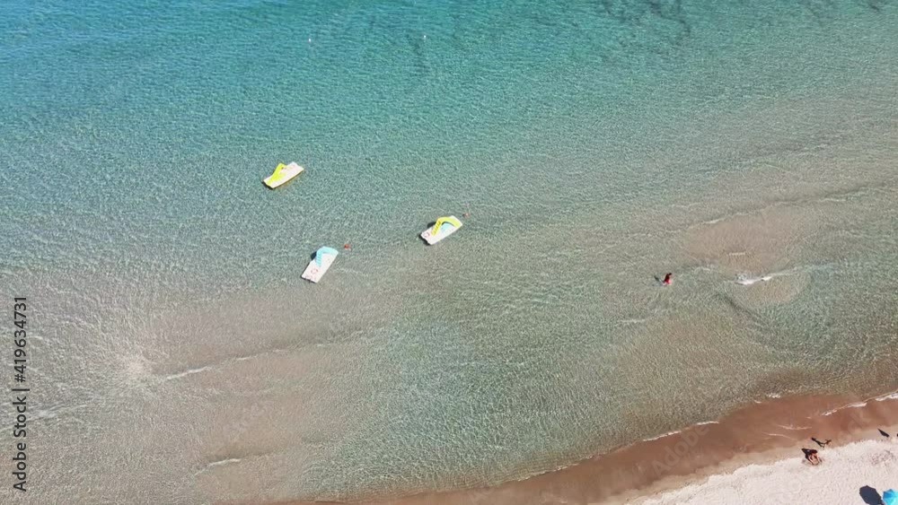 Top View Of The Beach With Tropical Crystal Clear Water Waves And People Walking On The Water's Edge On A Warm Sunny Day In Sardinia, Italy - Aerial drone static down view shot in slow motion Top View Of The Beach With Tropical Crystal Clear Water Waves And People Walking On The Water's Edge On A Warm Sunny Day In Sardinia, Italy - Aerial drone static down view shot in slow motion