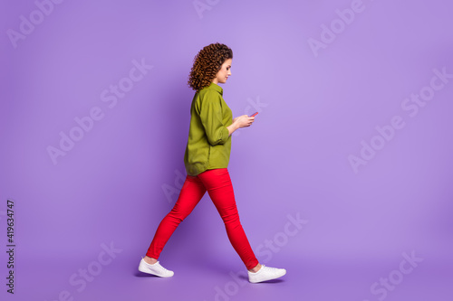 Full size profile side photo of young attractive pretty beautiful girl go walk using smartphone isolated on violet color background