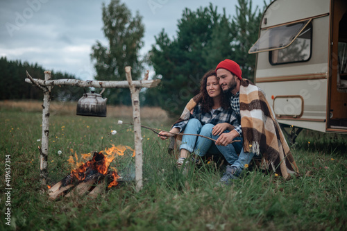 Couple in a checkered plaid roasting marshmallows on fire near the trailer home.