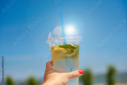 cool refreshing lemonade in hand. woman holding ice invigoration summer drink in transparent plastic glass