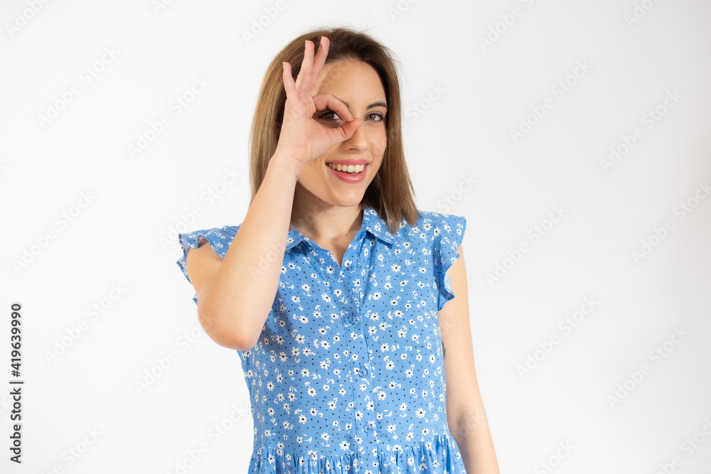 Young beautiful woman wearing casual dress standing over white isolated background smiling positive doing okay sign with hand and fingers. Successful expression. Young beautiful woman wearing casual dress standing over white isolated background smiling positive doing okay sign with hand and fingers. Successful expression.