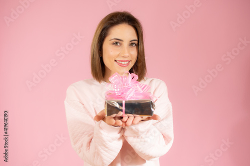 Happy smiling woman showing small gift box isolated over pink background.