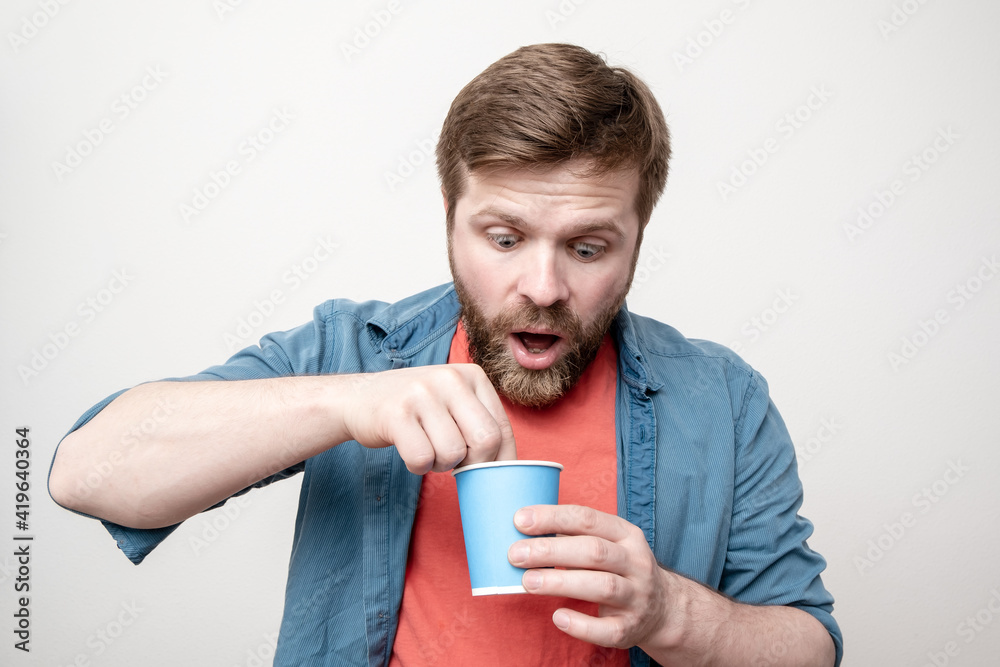 Shocked man with a paper cup in hand takes something out of freshly drunk tea with surprise. Concept of poor quality products. Shocked man with a paper cup in hand takes something out of freshly drunk tea with surprise. Concept of poor quality products.