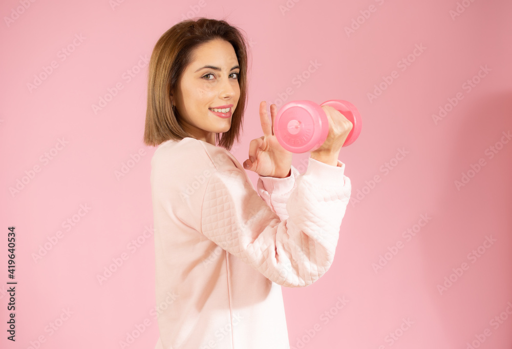 Beautiful young woman holding dumbbell isolated over pink background. Beautiful young woman holding dumbbell isolated over pink background.