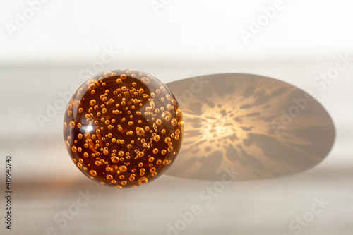 orange glass ball with air bubbles inside illuminated by sunlight on a white-gray background