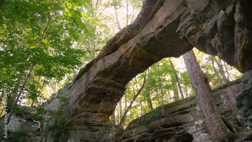 Cool adventure natural rock bridge in a fantastical forest ravine on a sunny spring day with sun peeking through, low angle tracking dolly shot, slow motion Cool adventure natural rock bridge in a fantastical forest ravine on a sunny spring day with sun peeking through, low angle tracking dolly shot, slow motion