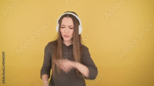 Young business woman 25 years old fun dancing in big white headphones on yellow background