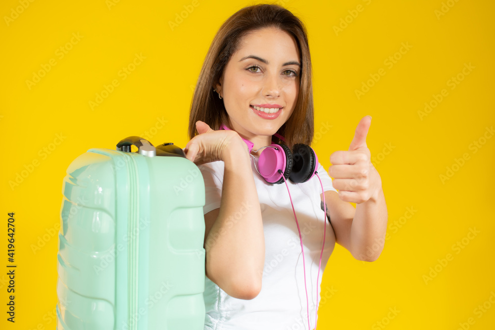 Young happy beautiful woman in headphones holding yellow suitcase over yellow background Young happy beautiful woman in headphones holding yellow suitcase over yellow background
