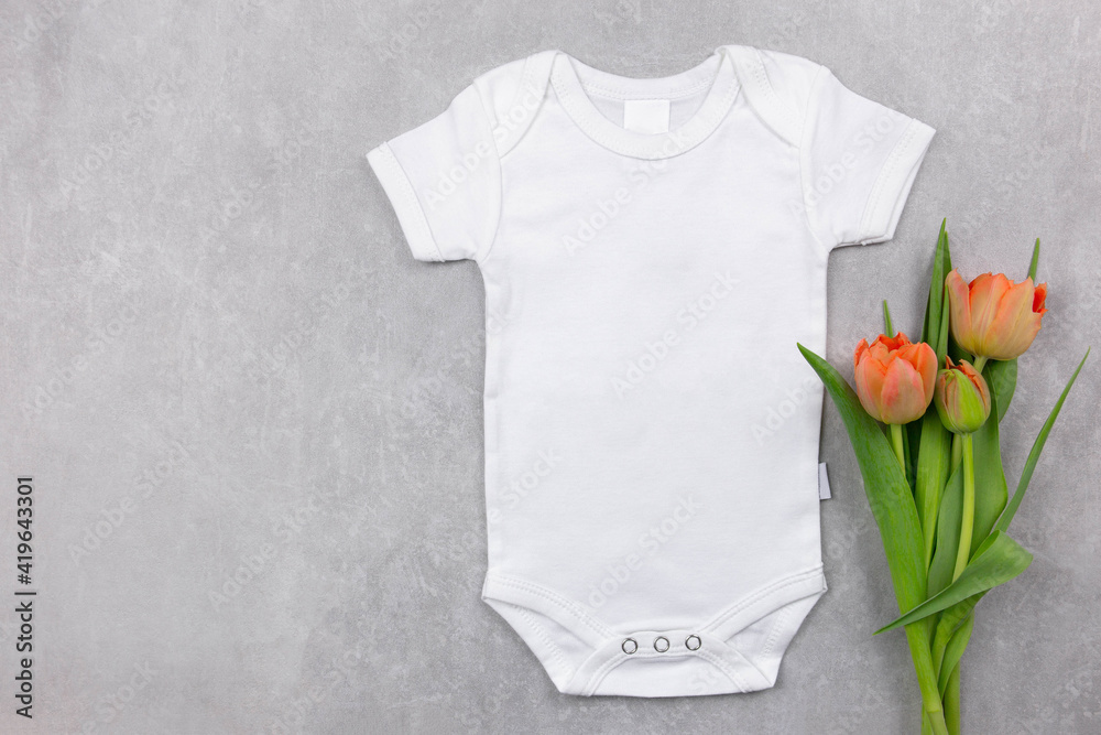 White baby girl or boy bodysuit mockup on the gray concrete background with  tulips flowers decoration. Design onesie template, print presentation mock  up. Top view. Flat Lay. Copy space. foto de Stock
