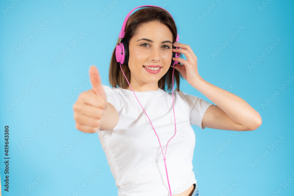 Smiling pretty young woman with headphones showing thumb up isolated over blue background Smiling pretty young woman with headphones showing thumb up isolated over blue background