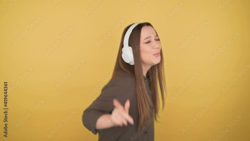 Young business woman 25 years old fun dancing in big white headphones on yellow background Young business woman 25 years old fun dancing in big white headphones on yellow background