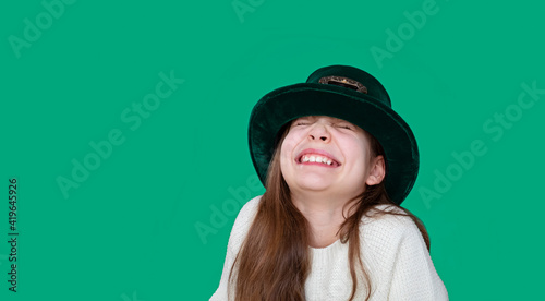 A closeup portrait of preteen girl in St. Patrick's Day hat on green backgroundwhite. Copy space