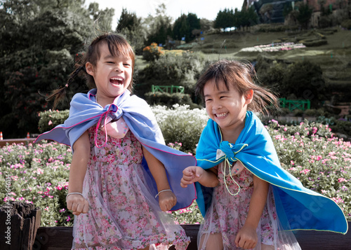 Fototapeta Two little girls in the shawl plays superhero smile happily in the garden