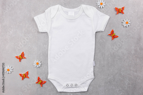 White baby girl or boy bodysuit mockup on the gray concrete background with daisy flowers and summer or spring decoration. Design onesie template, print presentation mock up. Top view. Flat Lay.