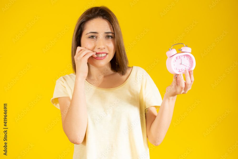 Portrait of worried young woman holding alarm clock isolated over yellow background Portrait of worried young woman holding alarm clock isolated over yellow background