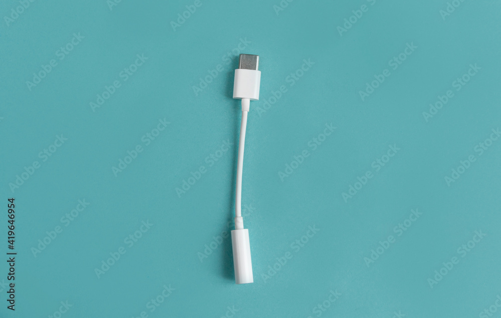 An adapter for a USB to 3.5mm type c headphone cable on a smartphone. White cable close-up, 3.5 mm audio cable on a blue background. view from above An adapter for a USB to 3.5mm type c headphone cable on a smartphone. White cable close-up, 3.5 mm audio cable on a blue background. view from above