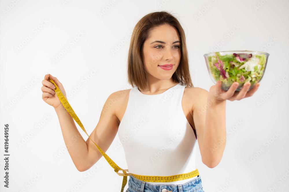 Young woman with measure tape showing a bowl of salad isolated over white background Young woman with measure tape showing a bowl of salad isolated over white background