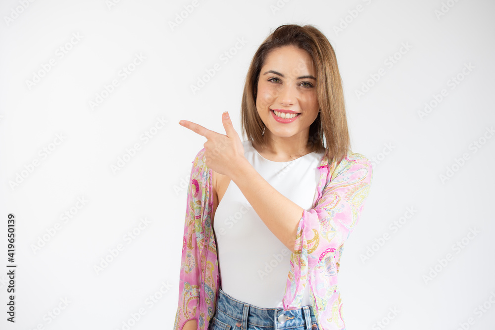Young beautiful woman over isolated background smiling and pointing with hand and finger to the side. Young beautiful woman over isolated background smiling and pointing with hand and finger to the side.