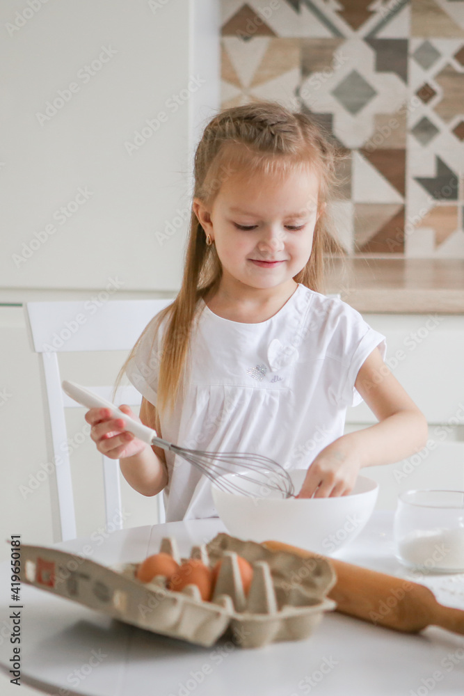 Portrait of a little cute smiling girl. Childrens hands kneading dough on the table in the art nouveau kitchen. Preparing for Easter baking. Biscuits. Portrait of a little cute smiling girl. Childrens hands kneading dough on the table in the art nouveau kitchen. Preparing for Easter baking. Biscuits.