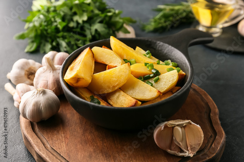 Bowl of tasty baked potato with garlic on dark background
