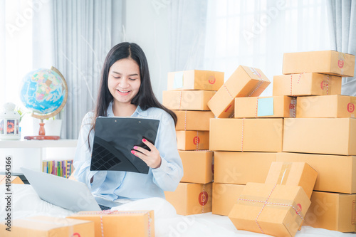 young Asian woman business worker are packing product to the box for sent to customer who order with online marketing, small business from home when self-isolated quarantine at home, work from home