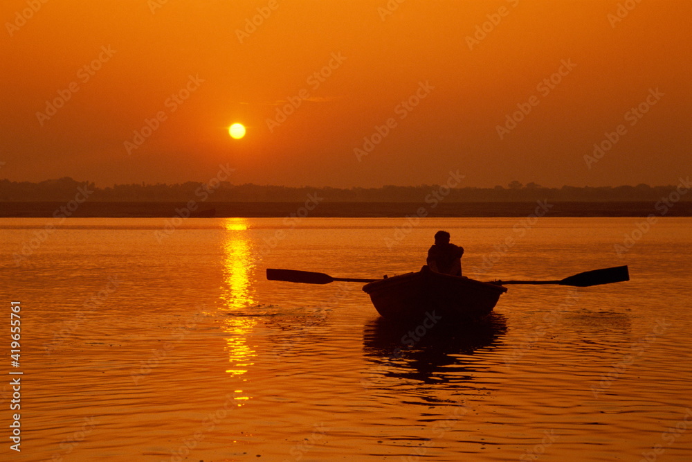 Figure in rowing boat silhouetted at sunset, River Ganges, Varanasi (Benares), Uttar Pradesh state Figure in rowing boat silhouetted at sunset, River Ganges, Varanasi (Benares), Uttar Pradesh state