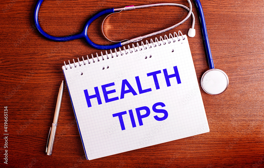 On a wooden table are a pen, a stethoscope, and a notebook labeled HEALTH TIPS. Medical concept On a wooden table are a pen, a stethoscope, and a notebook labeled HEALTH TIPS. Medical concept