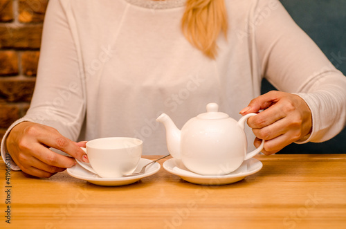 Young woman in a cafe drinks ginger tea and pours it from a teapot into a white cup on a saucer
