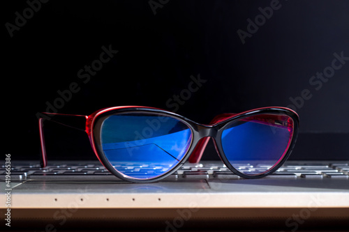 Red and black female glasses for working at a computer with a blue filter on the laptop keyboard. Anti blue light and rays. Eye protection