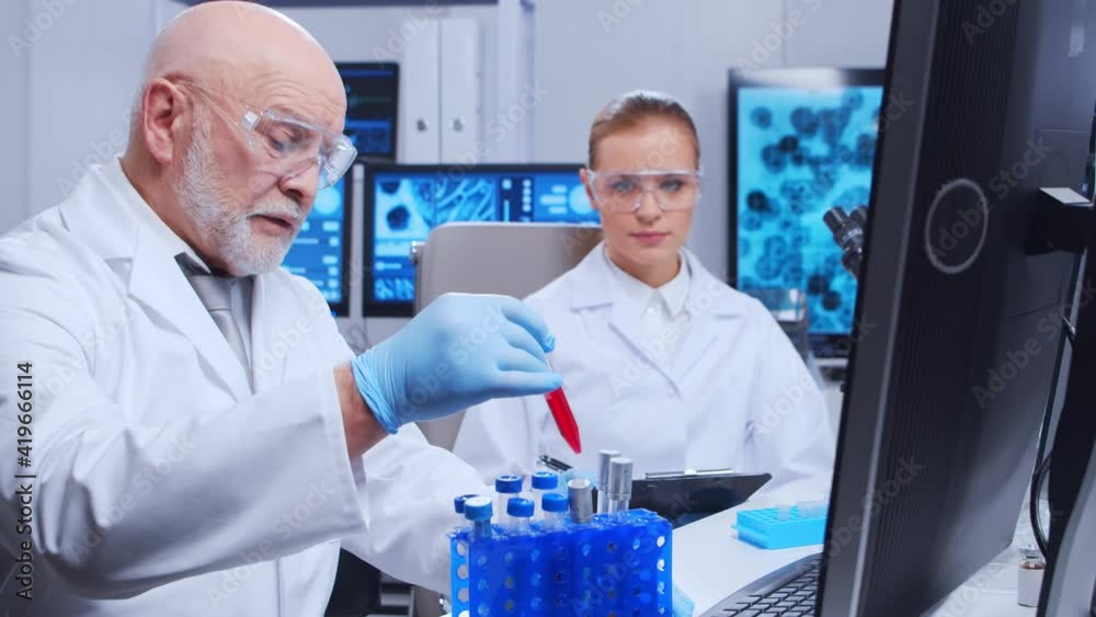 Elderly professor and young laboratory assistant are doing scientific experiment in a modern laboratory. Genetic engineers workplace. The concept of science, medicine and vaccine development. Elderly professor and young laboratory assistant are doing scientific experiment in a modern laboratory. Genetic engineers workplace. The concept of science, medicine and vaccine development.