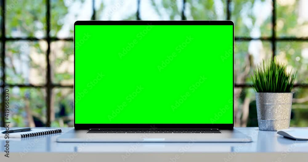 Laptop with blank green screen. Static footage with trees swaying or moving in the wind. Home interior or loft office background, 4k 24fps UHD, loop video