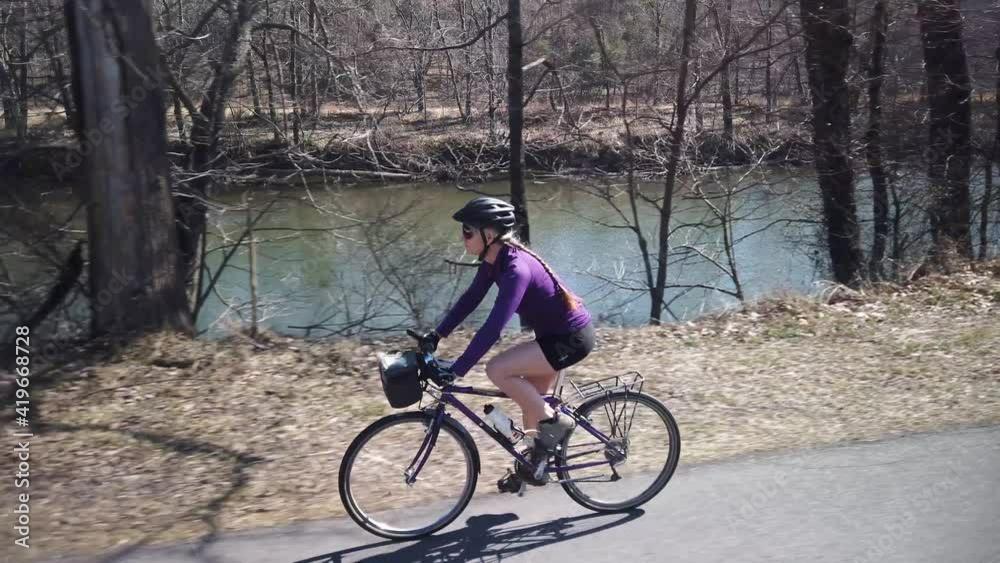 Closeup side view of happy mature woman biking along a river on a beautiful spring day with the sun shining. Closeup side view of happy mature woman biking along a river on a beautiful spring day with the sun shining.