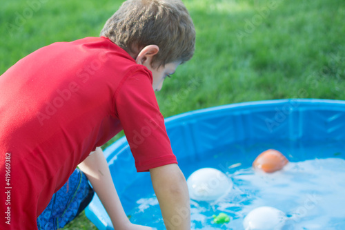 Boy with Autism doing sensory play: water balloons in a kiddie pool in the backyard