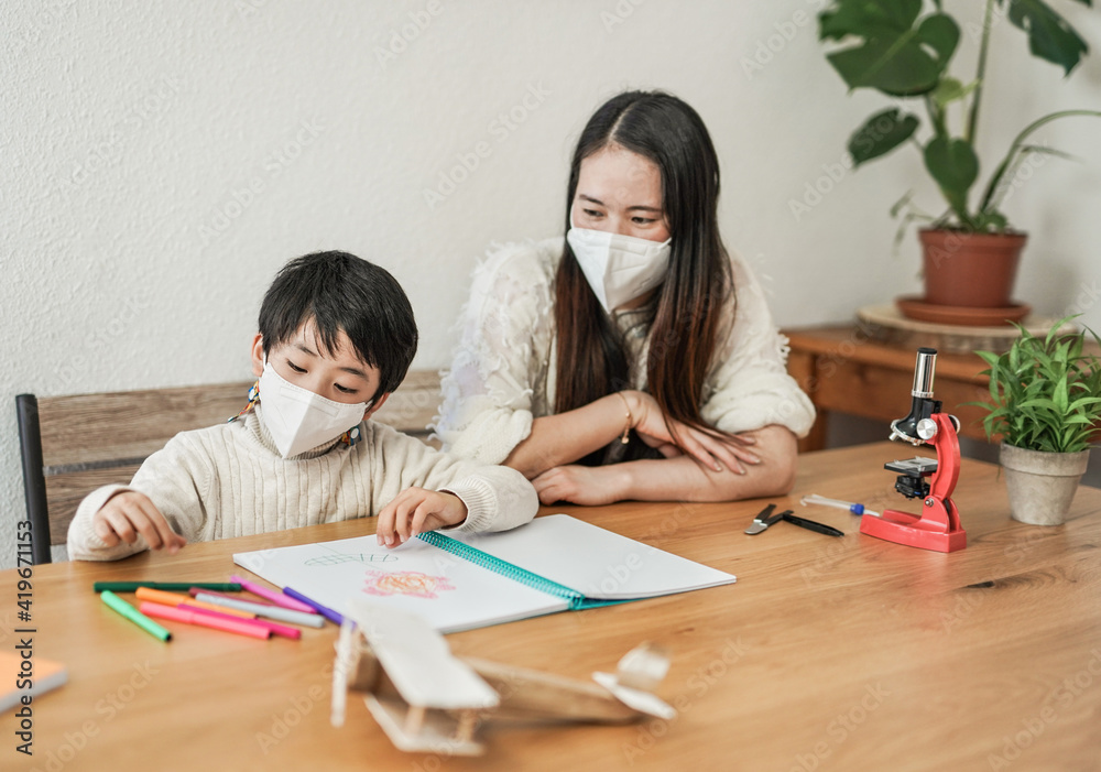 Asian nanny doing drawing activities with little kid while wearing surgical face masks for coronavirus outbreak - Preschool child painting flower - Daycare concept Asian nanny doing drawing activities with little kid while wearing surgical face masks for coronavirus outbreak - Preschool child painting flower - Daycare concept