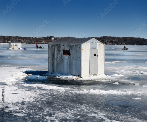 Ice fishing shacks on frozen Kempenfelt Bay of Lake Simcoe in winter with fishermen fishing and hauling a sled