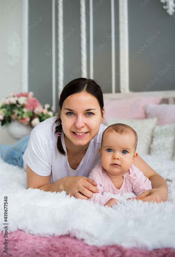 brunette mother and her daughter are lying on the blanket on the bed. Mom hugs baby girl brunette mother and her daughter are lying on the blanket on the bed. Mom hugs baby girl