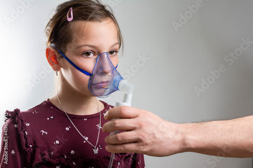 Little girl using inhaler at home and looking at camera. Little girl making inhalation with nebulizer at home. child asthma inhaler inhalation nebulizer steam sick cough concept Horizontal. 