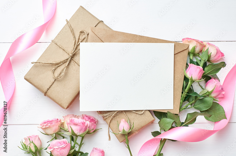 Greeting card with pink roses and gift boxes on white wooden background