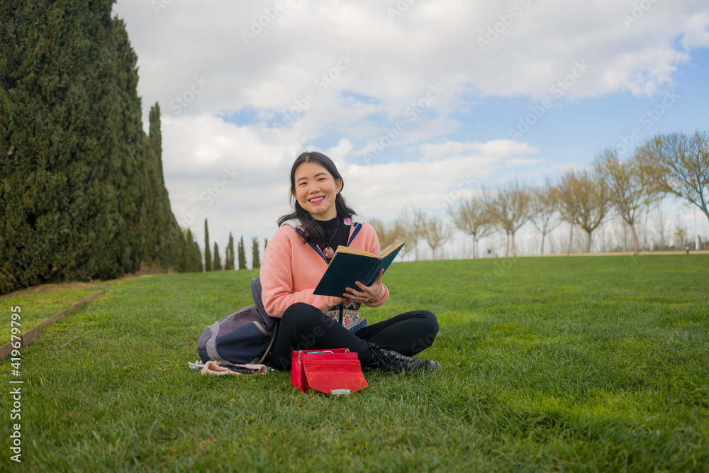 young Asian woman enjoying novel on grass - lifestyle portrait of young happy and pretty Japanese girl reading a book at beautiful city park in reading and studying concept young Asian woman enjoying novel on grass - lifestyle portrait of young happy and pretty Japanese girl reading a book at beautiful city park in reading and studying concept