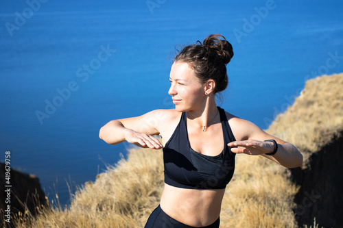 Young athletic woman runner doing exercise before jogging workout at mountain landscape nature path near blue sea. Summer morning stretching outdoors. Weight loss cardio goal achievement challenge