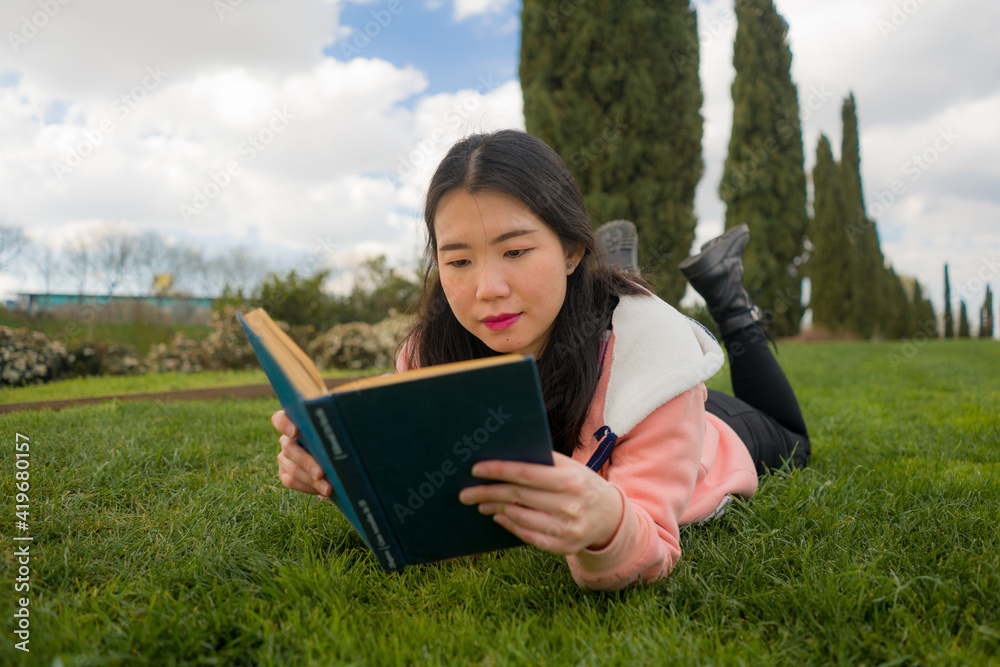 young Asian woman enjoying novel on grass - lifestyle portrait of young happy and pretty Korean girl reading a book at beautiful city park in reading and studying concept young Asian woman enjoying novel on grass - lifestyle portrait of young happy and pretty Korean girl reading a book at beautiful city park in reading and studying concept